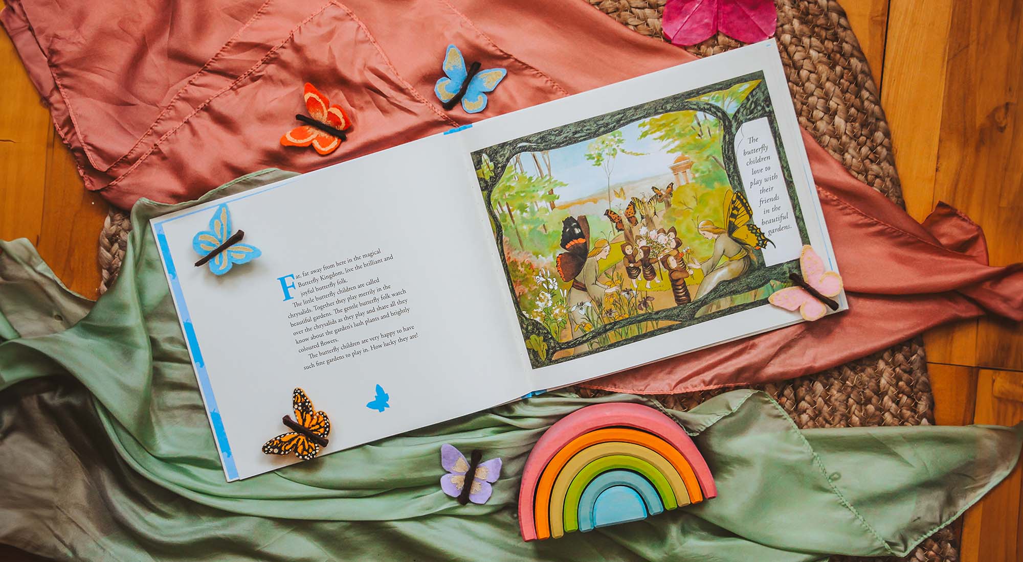 Butterfly Children book open laying on playsilks with a rainbow and felt butterflies.