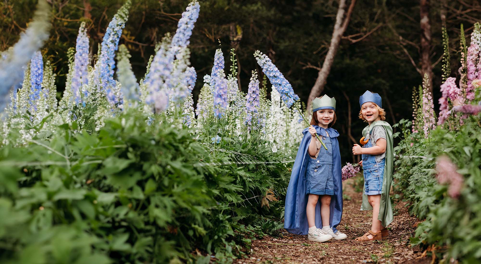 Two kids are dressed in play silks running through a field of flowers