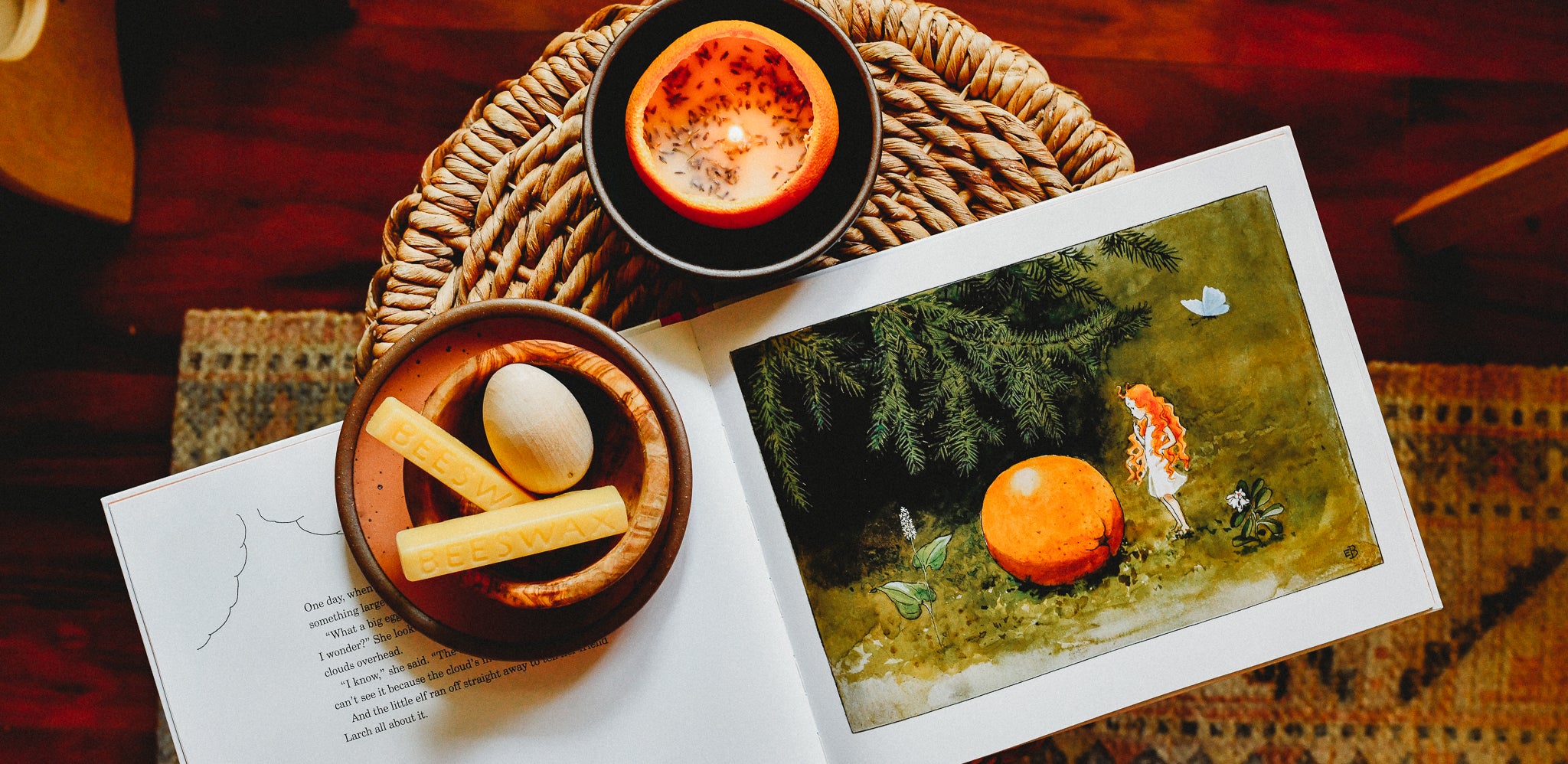 Orange peel beeswax candle lit on a table next to an open book, The Sun Egg by Elsa Beskow.