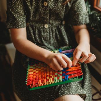 A child weaving a potholder loom to craft.