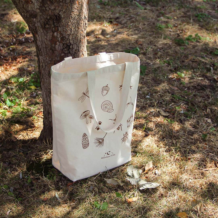 Nature Treasure Hunt Canvas Book Tote outdoors, next to a tree.