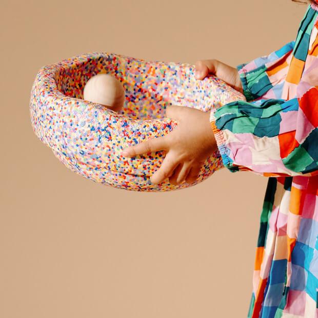 A child rolls a wooden ball inside of a Stapelstein super confetti stepping stone.