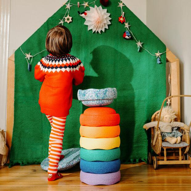 A child steps onto the super cool balance board to hang a holiday decoration. The Stapelstein stepping stones are stacked up next to them.