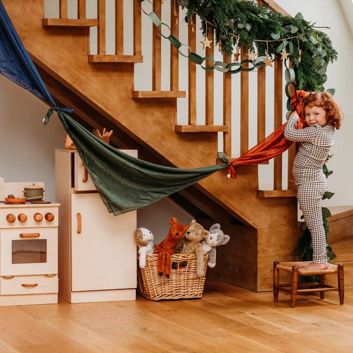 A girl hanging a pennant banner made from the Bella Luna Toys 2024 Holiday Playsilk Collection.