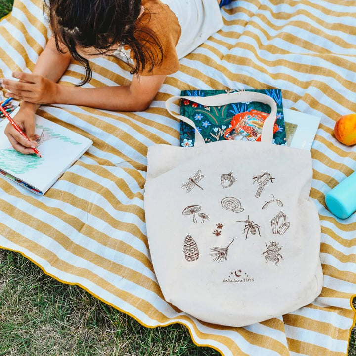 Bella Luna Toys Nature Hunt Book Tote on a picnic blanket with a child drawing.