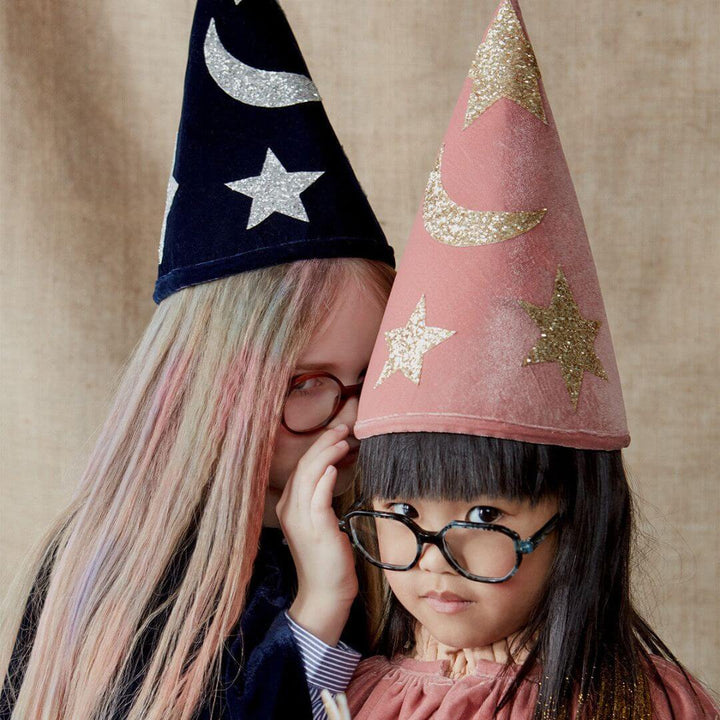 Two children sharing a secret while wearing Meri Meri velvet wizard costumes.