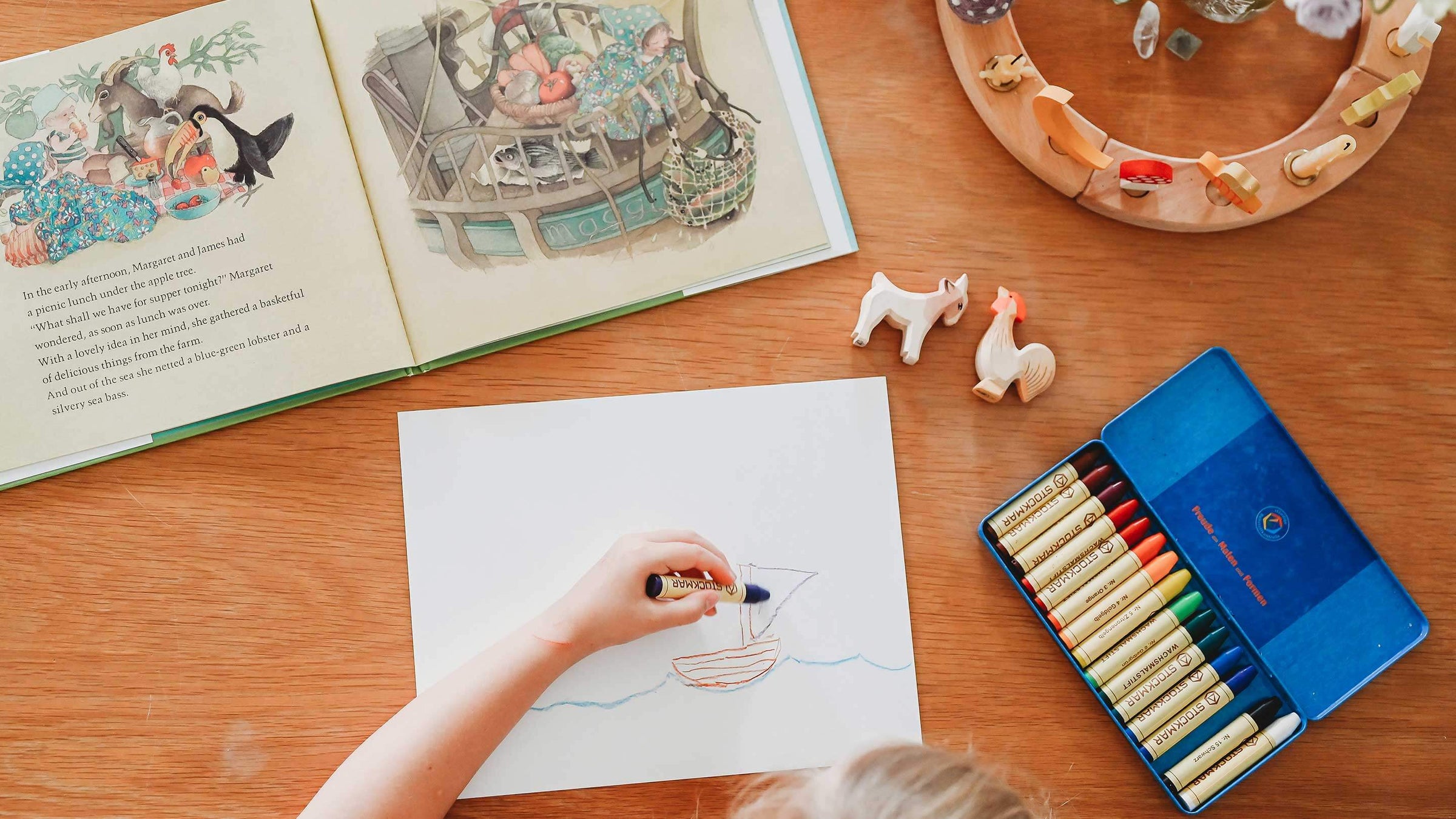 Child drawing sailboat with stockmar crayons on wooden table