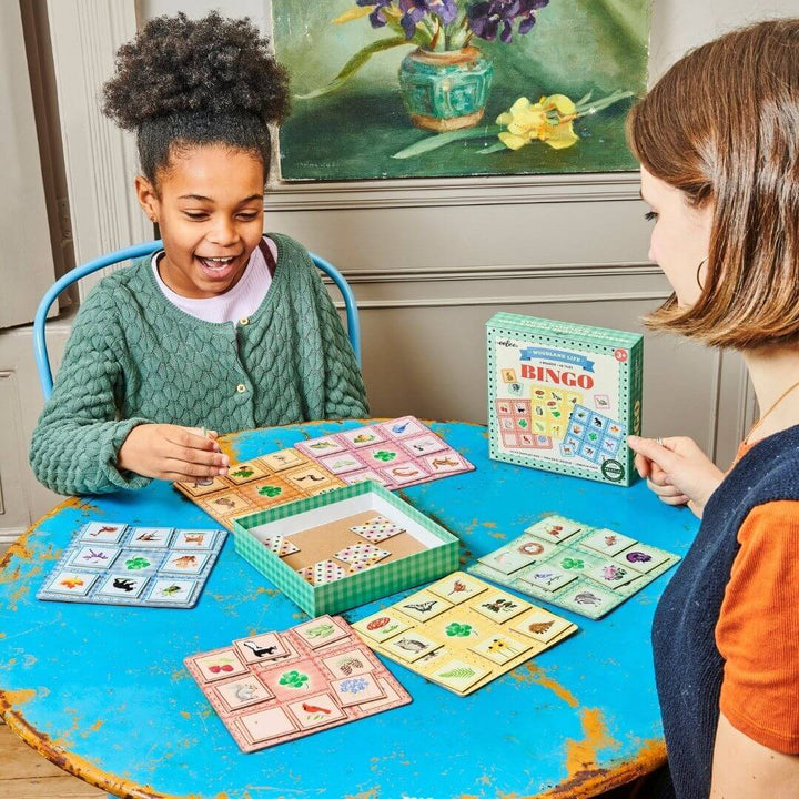 A child and adult at a table play Busy Woods Bingo game by eeBoo.