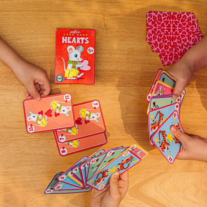 An overhead view of two children's hands holding the eeBoo Hearts cards as they play the game.