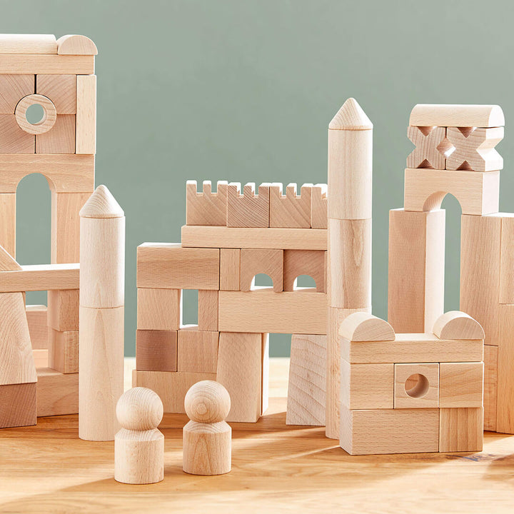 Basic Building Blocks 102 Piece Extra Large Wooden Starter Set arranged in various structures, accompanied by two wooden figures, on a table.