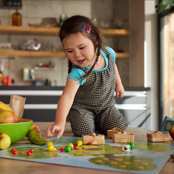 Girl in pigtails and checkered jumper playing HABA's Orchard Board Game on kitchen table