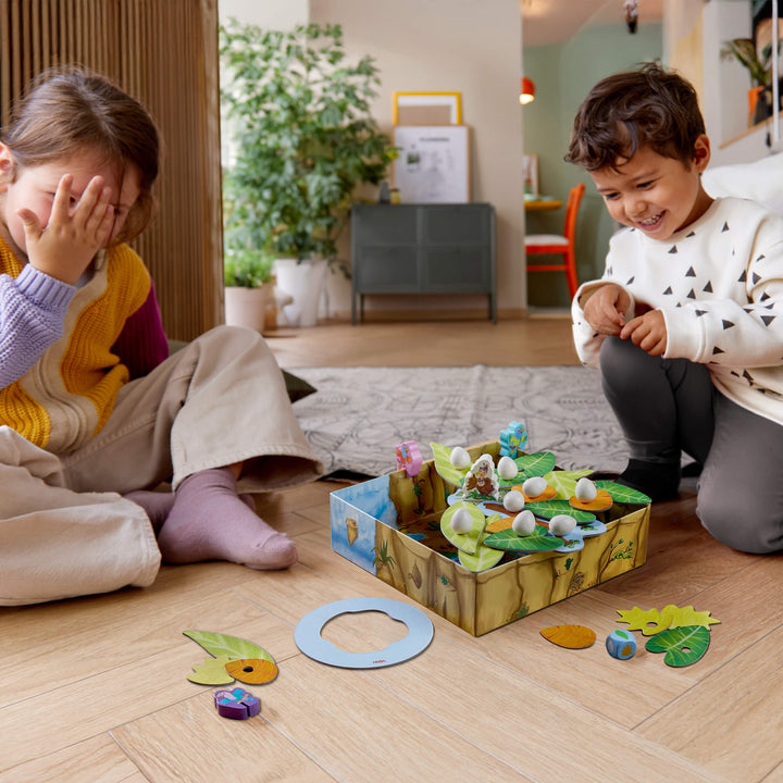 Two children laughing while playing the nest building and balancing game Teetering Treetops from HABA.