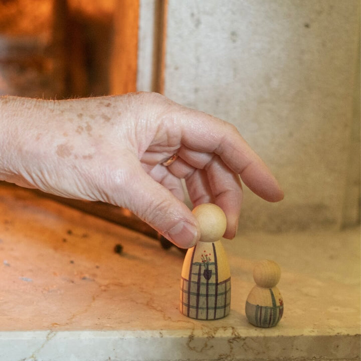 A hand holds a wooden figure with an apron next to a matching child figure from the 2024 Grapat Advent Calendar.