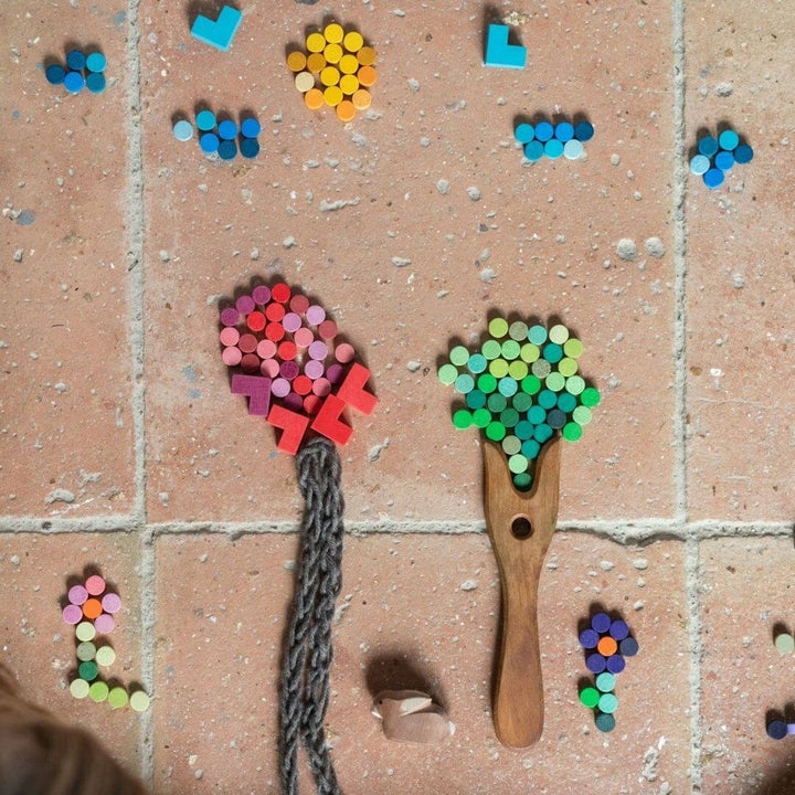 Grapat Bloom Wooden Mosaic Set – Hand-painted wooden pieces  are arranged to look like trees and flowers and different designs on a brick patio for open-ended play, pattern-making, and creative exploration.