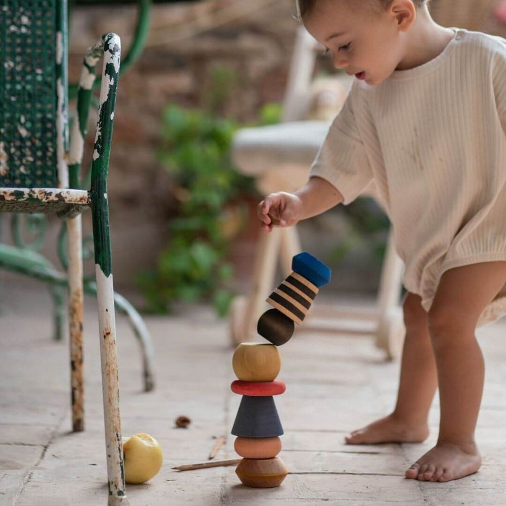 Young child setting up the Serendipity Wooden Stacking Toy from Grapat. This colorful handcrafted wooden stacking toy with 8 unique pieces is perfect for open-ended play and creative building fun.