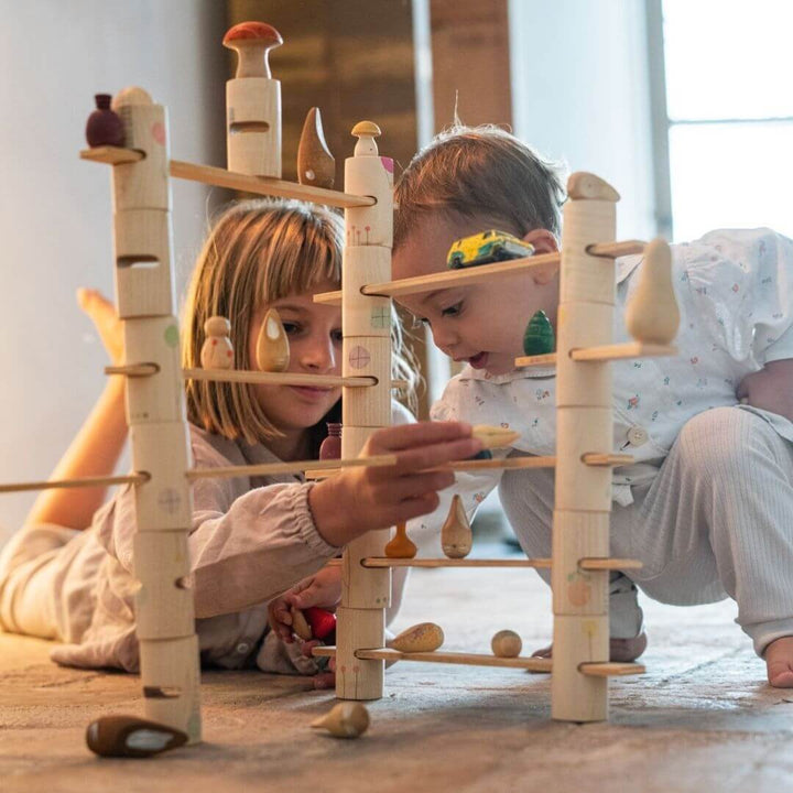 Two children playing with the Grapat Woodland Stacking Tower Set with hand-painted wooden tubes and walkways, with lots of other types of toys stacked on the wooden walkways showing open-ended building and imaginative play.