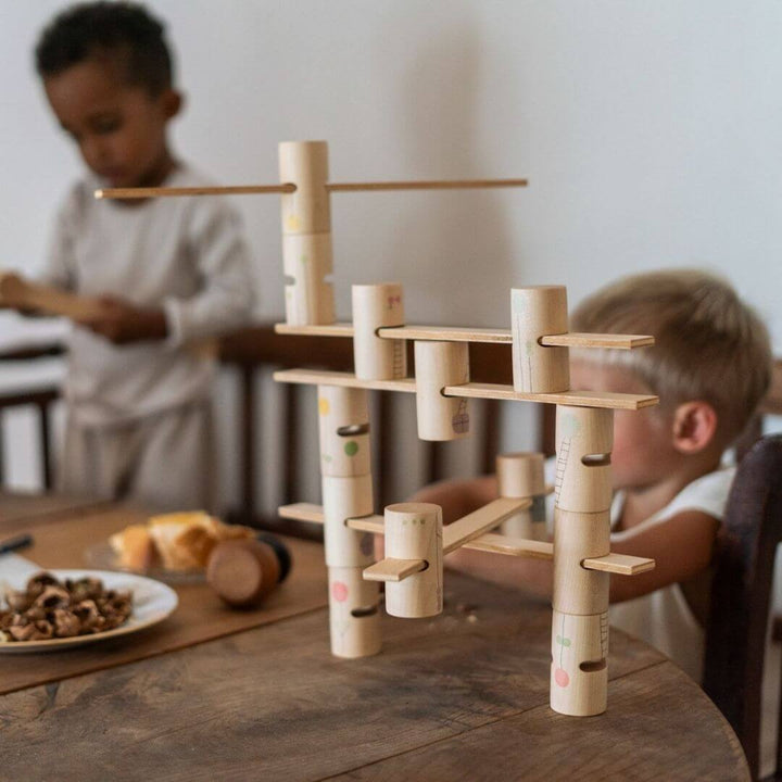 Two children have made a giant Grapat Woodland Stacking Tower with the hand-painted wooden tubes and walkways, designed for open-ended building and imaginative play.