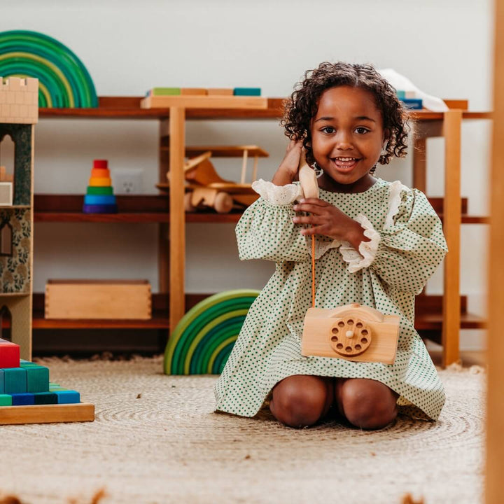 A child "talking" on their wooden telephone from Grimm's Wooden Toys.