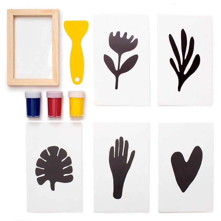 Kikkerland Make Your Own Screen Prints kit with yellow, red, and blue jars of paints, yellow scraper, natural wooden frame with clear acrylic film, and 5 black and white prints