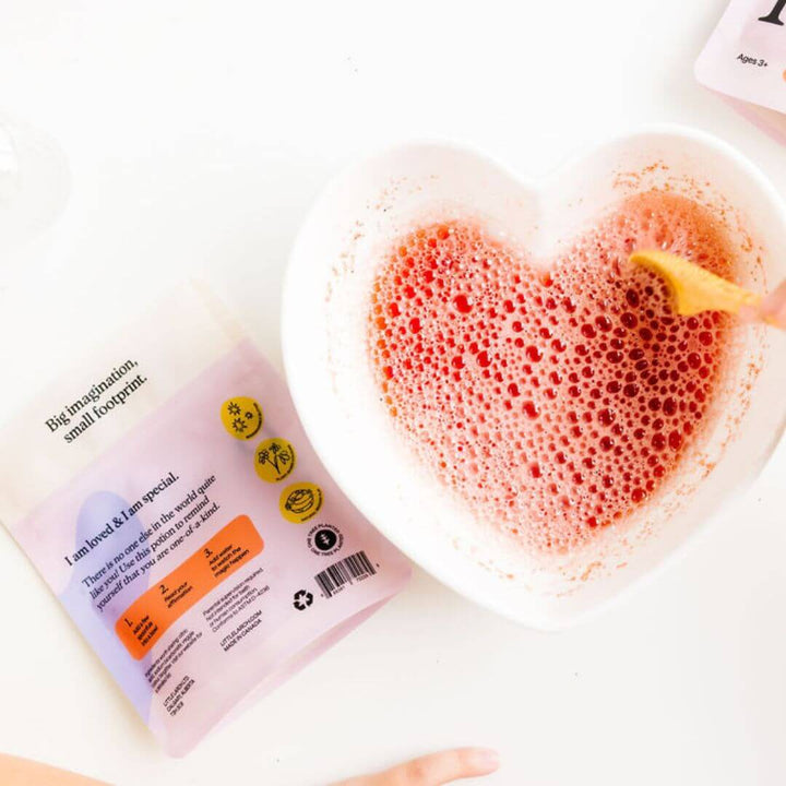 A bubble pink potion being mixed in a heart shaped bowl. The back of the Little Larch Love Spell Potion Play can be seen on the table next to the bowl.