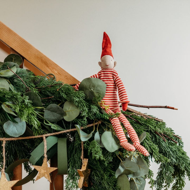 Maileg Long Legged Pixy sits on holiday greenery.