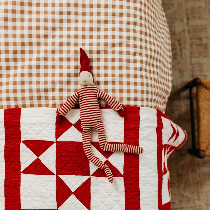 Maileg Long Legged Pixy laying on a child's bed with a red and white quilt.