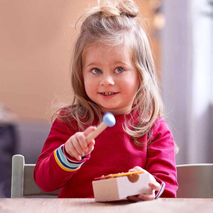 Child in red sweatshirt playing with metallophone and mallet