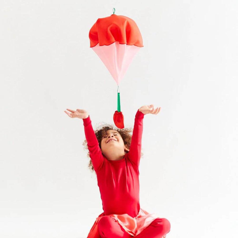 A child in red pajamas trying to catch the foating silk strawberry parachute.