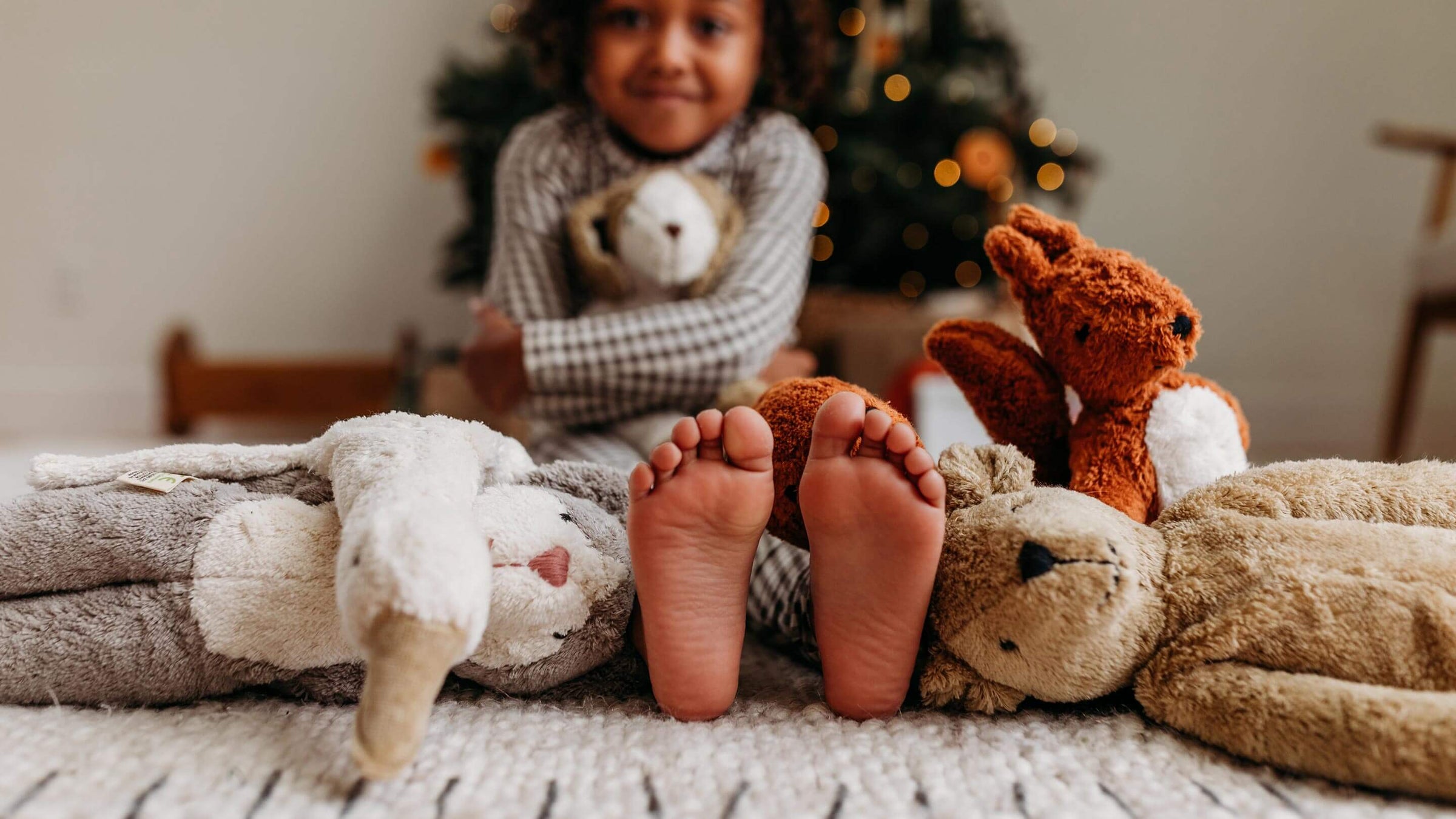 Child's feet covered in Senger stuffed animals on a white rug