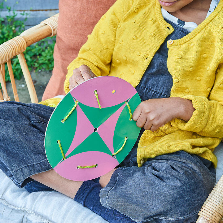 Child lacing a large round pink and green pattern card