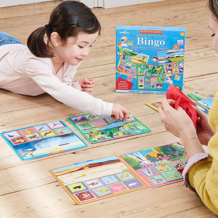 Girl laying on a wooden floor playing Where Do I Live? Bingo with mother